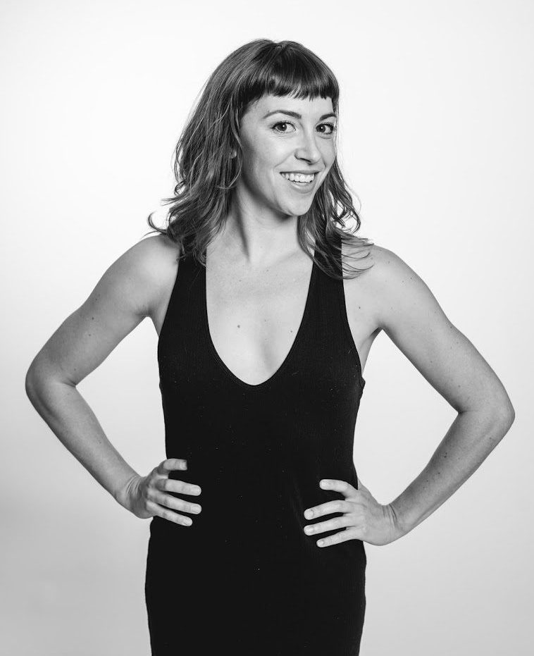 Black and white headshot of Veronica DeWitt standing, smiling with her hands on her hips.